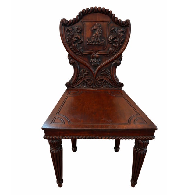 A fine and unusual pair of English William IV carved mahogany hall chairs. The chairs have shield form heraldic backs with...