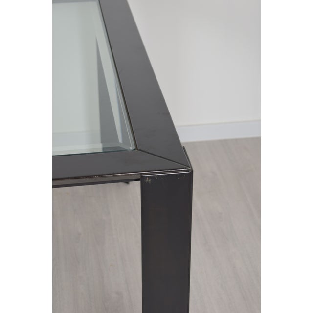 A 1970s Italian table with a simple, modern design, featuring a lacquered wood frame and glass top. The clean, geometric...