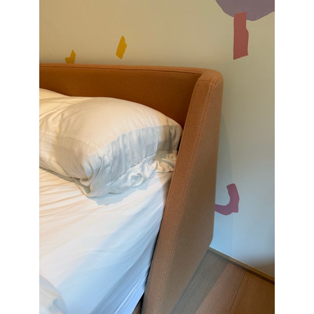 The Nook Queen Bed by Blu Dot features a distinctive wraparound headboard that curves gently into the upholstered frame,...