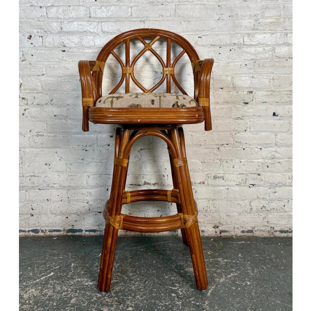 This is a rattan barstool with a palm tree upholstered cushion. With a rounded back and a solid rattan frame this...