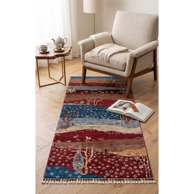 A hand-knotted runner in the Persian Gabbeh style, woven as a landscape in deep burgundy, indigo, camel and soft mauve....