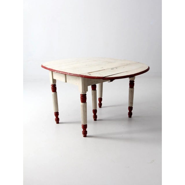 An antique drop leaf table with five legs circa early 20th century. The heavy wooden table features fluted legs and metal...