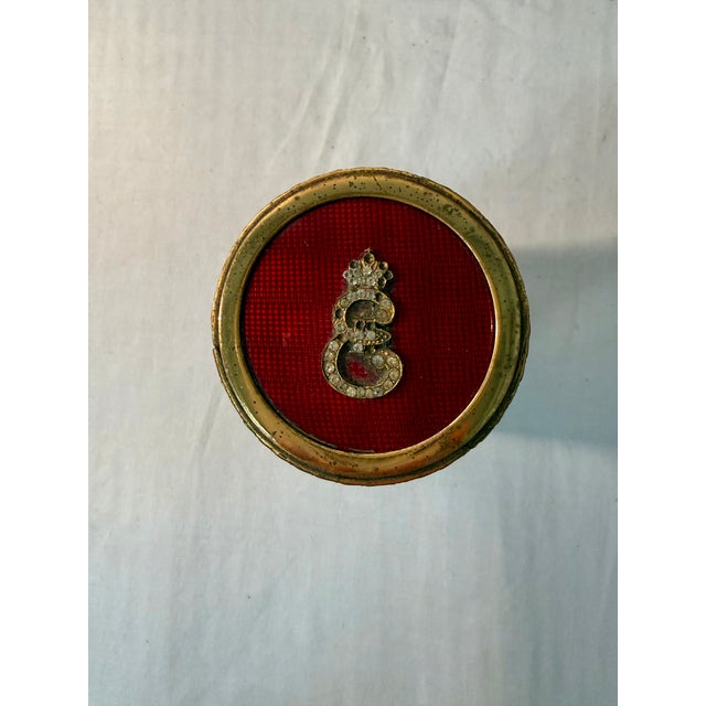 This unique cylindrical box, monogrammed with the letter "E," is crafted from red enamel and adorned with stones and...