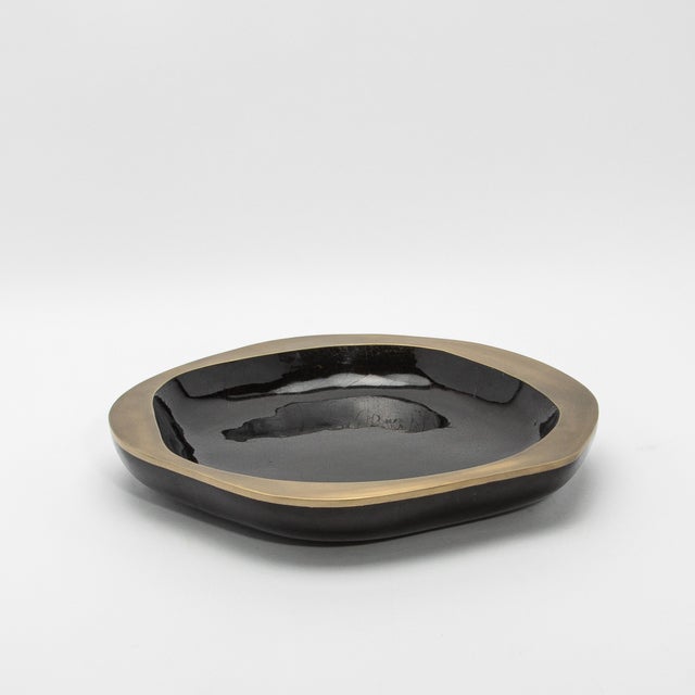 The Lily Bowl in black shell with bronze patina brass details by R&Y Augousti exudes refined elegance through its fusion...
