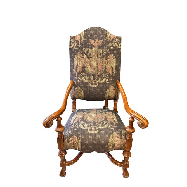 This striking pair of upholstered armchairs features beautifully carved wooden frames paired with richly detailed heraldic...