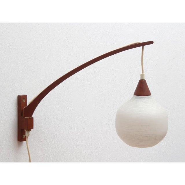 60s wall lamp. Swiveling arm, teak massive. Drop -shaped glass shade made of opal glass, slightly structured. (Diameter...