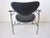 A black wrought iron framed lounge chair having black leather strap arms and brass hardware with the seat back and bottom...