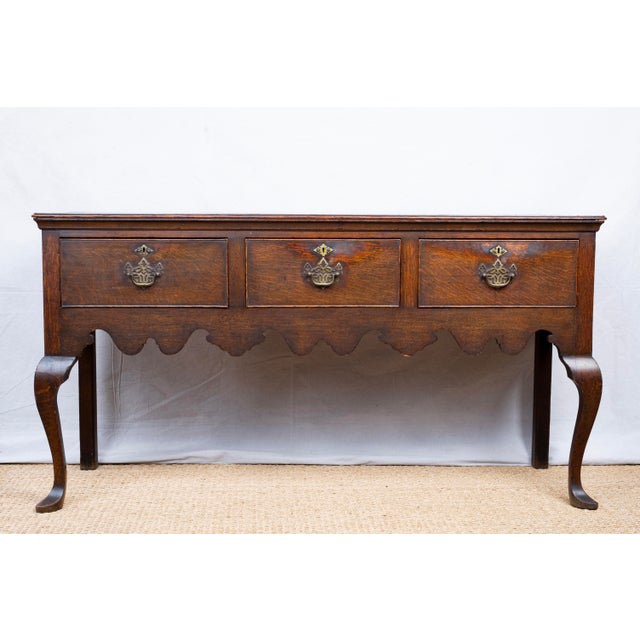 An antique oak console or dresser base, c. 1860, English. Featuring three drawings with original brass hardware and a...