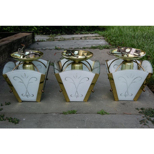 Mid Century Modern set of three flush mount ceiling fixtures with frosted white glass and gold metal frames. Each light...
