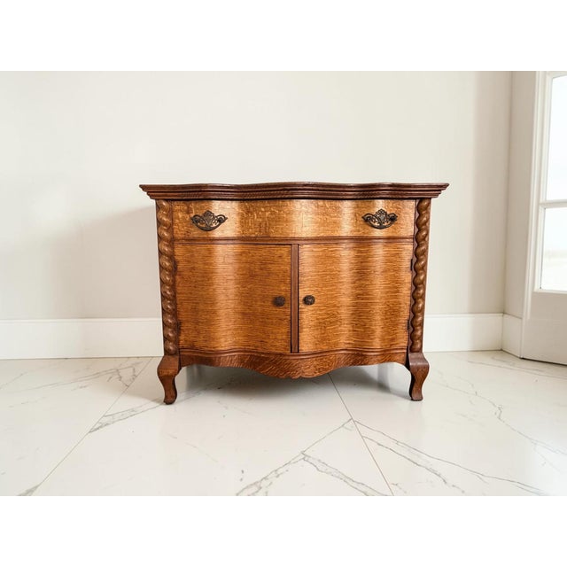 Beautiful antique solid oak cabinet featuring a striking serpentine front, rich quarter-sawn (tiger oak) grain, and carved...