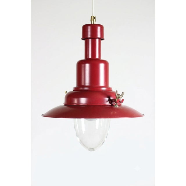 Red metal pendant light with industrial nautical style. Single light fixture with red exterior and brass details and a...