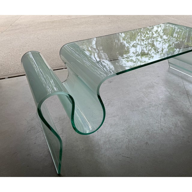 A striking vintage bent glass coffee table featuring a sculptural undulating silhouette and seamless waterfall form....