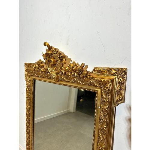 Elegant antique-style mirror with a richly detailed gilt frame. The top features an ornate crest with floral and scroll...