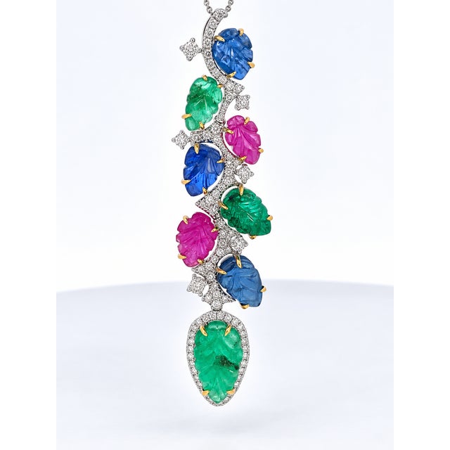 A vibrant tutti-frutti style pendant featuring an alternating cascade of hand-carved sapphires, emeralds, and rubies, each...