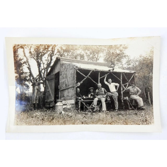 Vintage circa 1920 snapshot photograph of a group of men at a rustic camp cabin or shed. Looks like breakfast time, album...