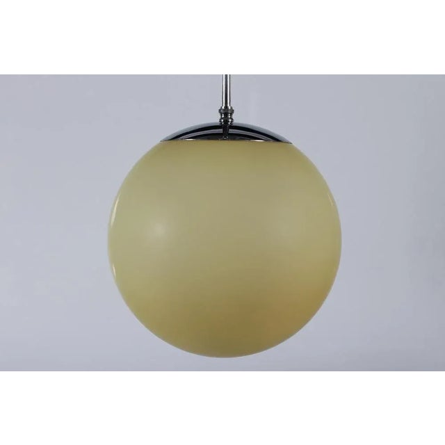 Original Art Deco pendent light with ball-shaped shade of matte light yellow glass made in the 1930s. The shade is mounted...