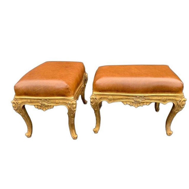 Elegant pair of hand-carved Italian benches, richly gilded and upholstered in supple brown leather. The frames showcase...