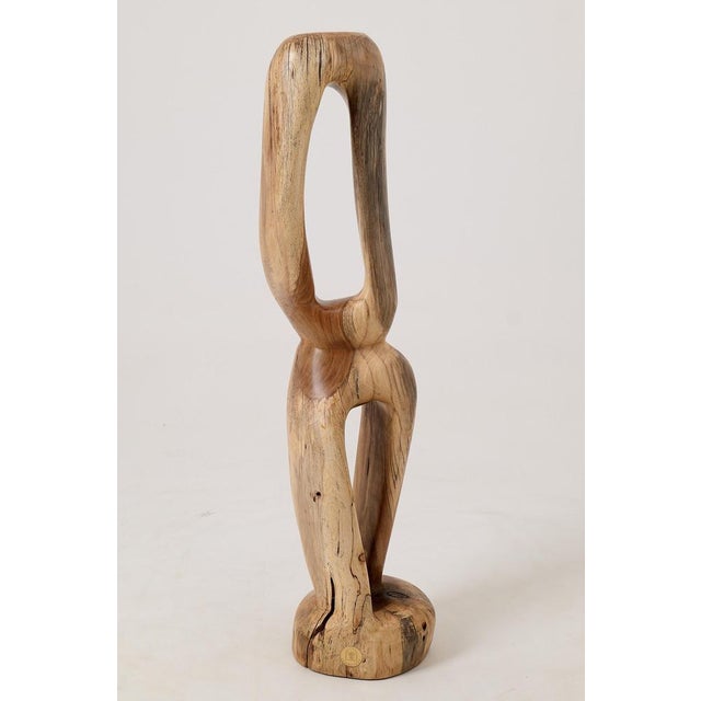 A sculpture carved from a single solid log, the form is abstract and figurative at the same time, suggesting a figure, a...
