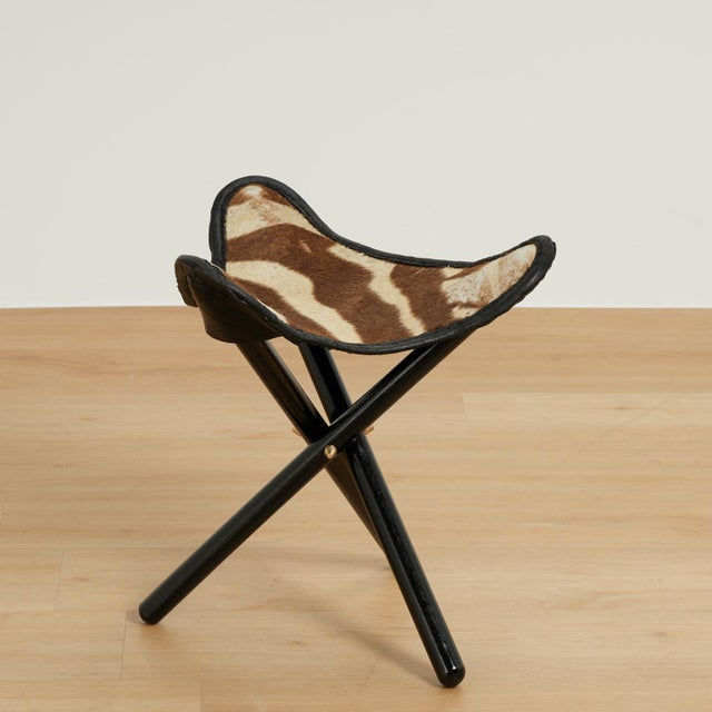 Chic safari style bench crafted with an organic zebra hide fitted on a folding tripod ebonized hardwood base.
