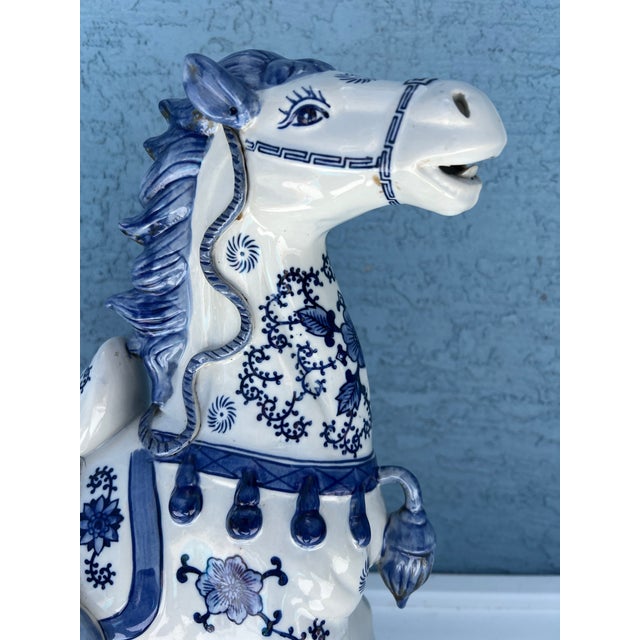 Vintage blue and white ceramic Tang style horse figurine featuring intricate floral patterns and caparisoned details. The...