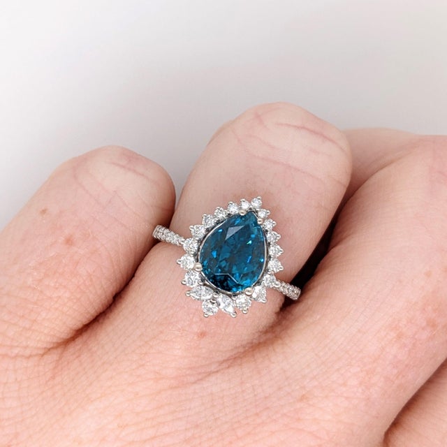 A blue zircon glows in a brilliant electric blue at the centre of this solid 14K white gold ring, surrounded by thirty-...