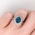 A blue zircon glows in a brilliant electric blue at the centre of this solid 14K white gold ring, surrounded by thirty-...