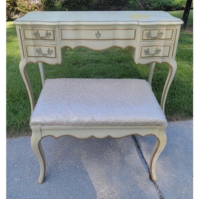 French Provincial vanity with flip top mirror and padded bench with cream painted finish and elegant gold detailing. Made...