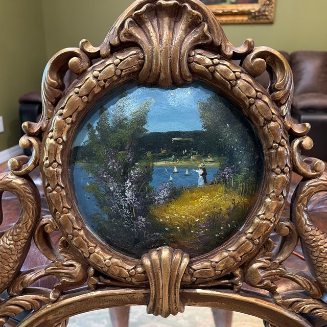 Semi-ornate gold wood frame mirror with three painted landscape scenes, shell and bird motifs. It's sort of an oval shape.