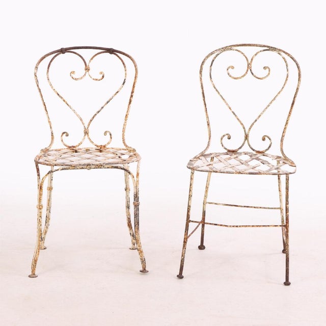 A charming set of four French garden chairs, circa 1950, crafted in wrought iron with graceful open scrollwork detailing...