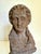 Here is a late 20th century neoclassical-style female bust sculpture with a weathered terracotta finish and textured cast...