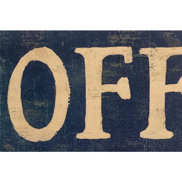 A weathered wooden directional sign reading "OFFICE" with a shaped scalloped border and painted dark charcoal with cream...