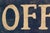 A weathered wooden directional sign reading "OFFICE" with a shaped scalloped border and painted dark charcoal with cream...