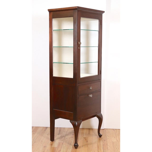 Vintage mahogany medical display cabinet in dark wood tones with glass shelves. Built tall and narrow to fit into tight...