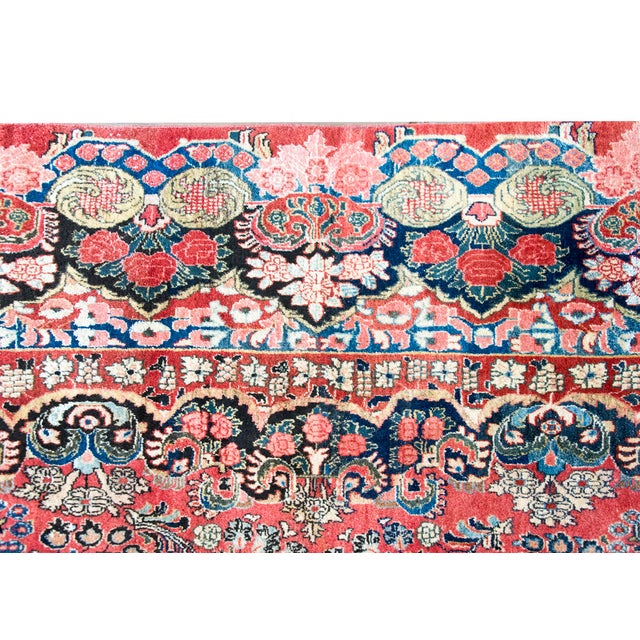 This antique Persian Sarouk rug, dating to the 1930s, features a classic all-over floral design on a rich red field. The...