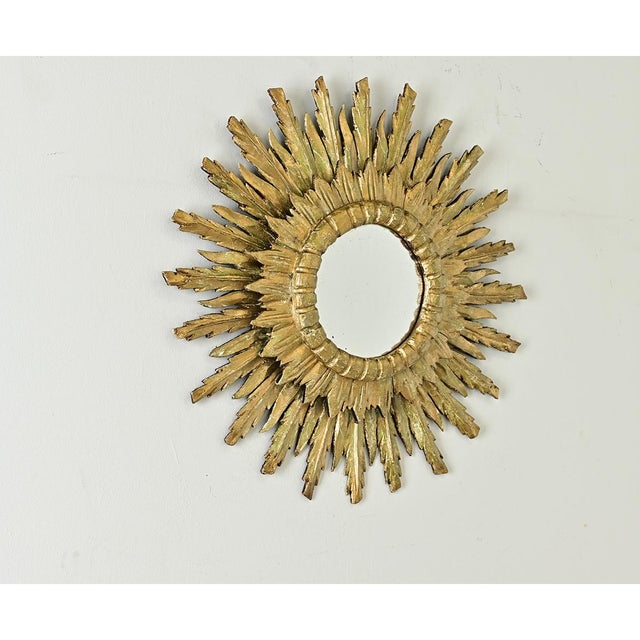 Dramatic feathered carvings of giltwood animate this antique Italian starburst mirror, the rays stretching upward and...
