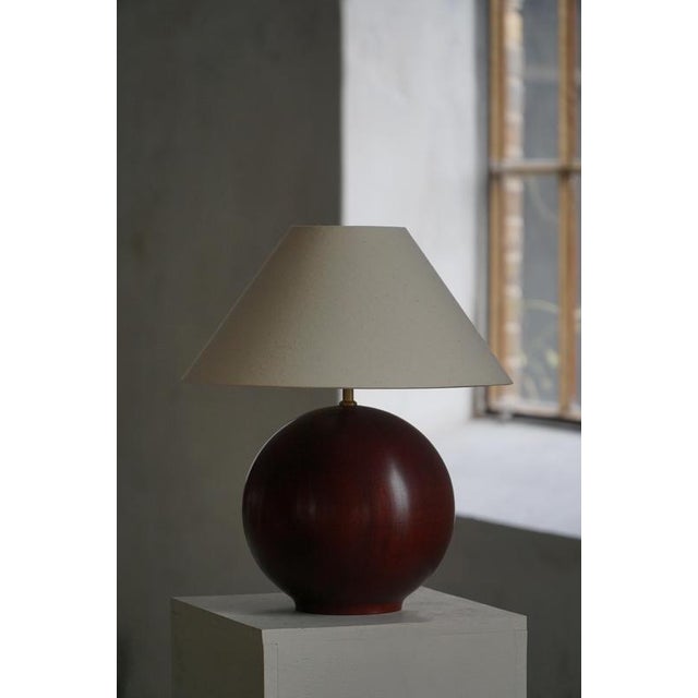 A sculptural table lamp crafted in dark stained beech wood with a warm reddish gloss, featuring a smooth, sphere-shaped...