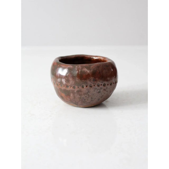 This vintage studio pottery bowl features an earthy brown glaze with subtle red undertones and a soft metallic sheen from...