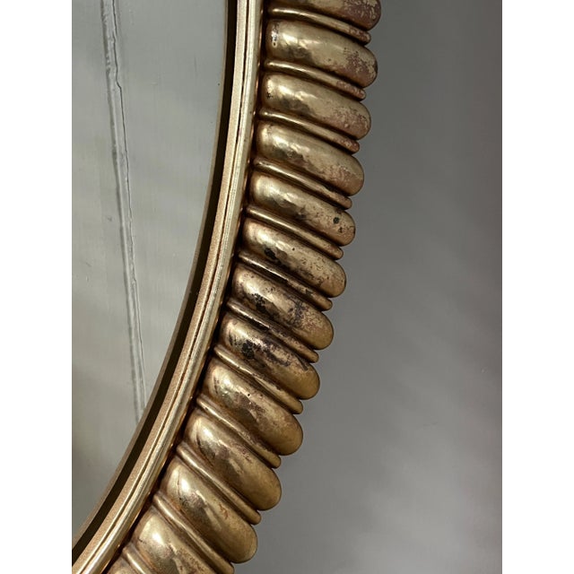 A single large vintage oval shaped wall mirror featuring a shaped array frame with a mottled metallic gold finish.