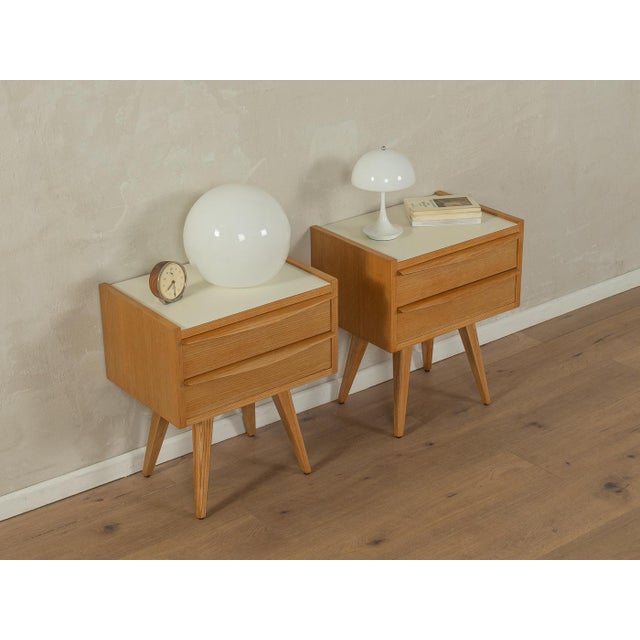Charming bedside tables from the 1950s. Ash veneer frames, each with two drawers and angled legs. The tops are covered...