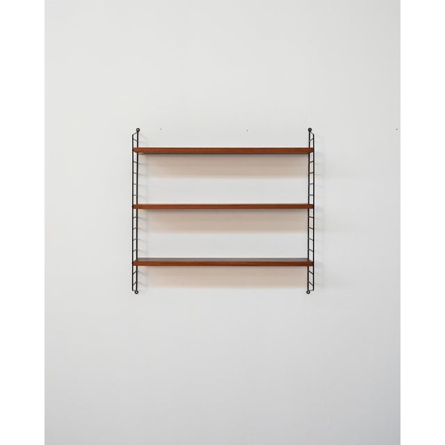 Modular structure in black lacquered metal with three teak shelves. Original label present. Designed by Nisse Strinning...