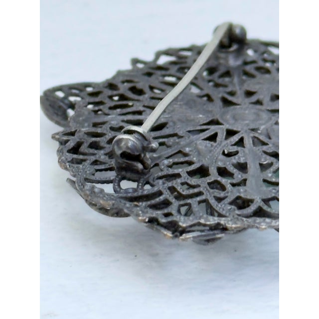 Vintage statement brooch featuring an openwork floral design centered by an oval green cabochon. Intricate filigree...