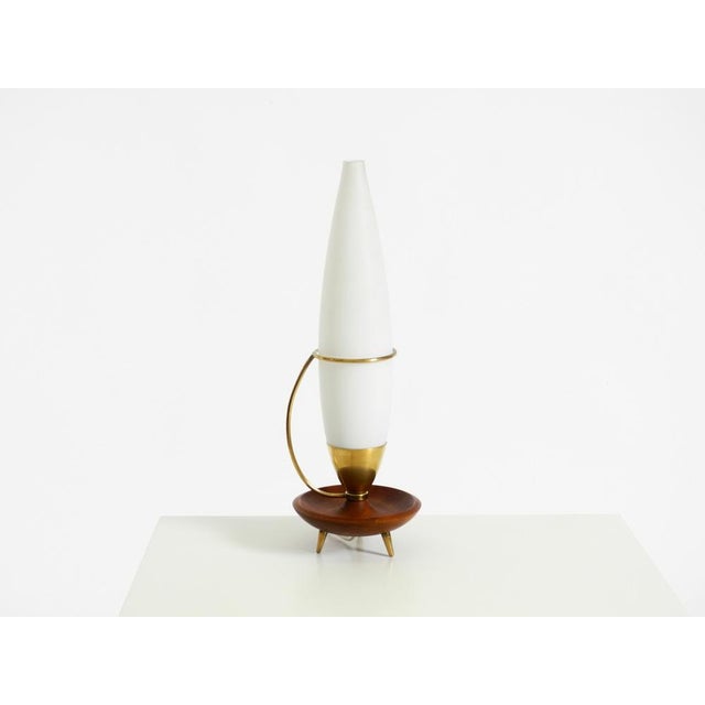 A beautiful, large mid-century modern tripod table lamp. Crafted from brass and teak, featuring a long milk glass shade. a...