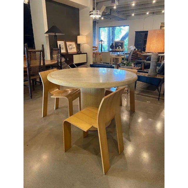 Round travertine and rattan pedestal base dining table. Pale ribbed rattan wraps the pedestal base and rolled edge of the...