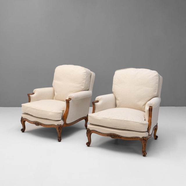 Pair of early 20th century French upholstered armchairs in beige fabric. Carved walnut show wood on cabriole legs. France...
