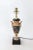 This vintage cream colored trophy cup lamp has leaf handles and a ring of foliage in gold color, with a small painting of...