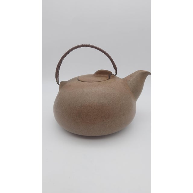 Organic-form stoneware teapot with a low rounded body, integrated spout, recessed lid, and wrapped swing handle. Finished...