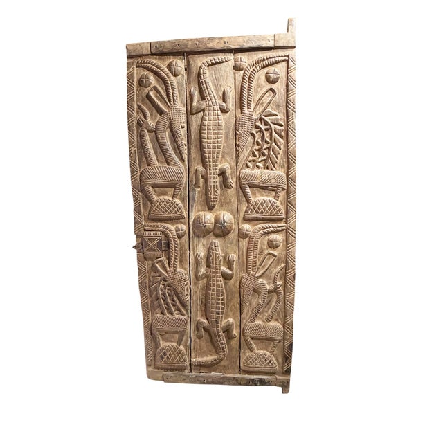 This vintage Dogon granary door from Mali showcases exceptional carved relief artistry, featuring four standing chiwaras...