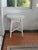Vintage white wicker round side table equipped with a protective inset glass top surface. Table has top tightly braided...