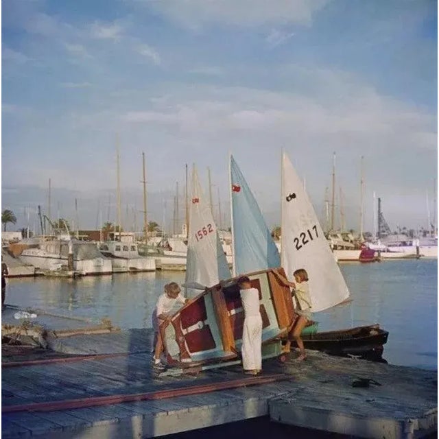 Sailing Dinghy 1956 by Slim Aarons Slim Aarons Limited Estate Edition A boy and two girls lifting a sailing dinghy off its...