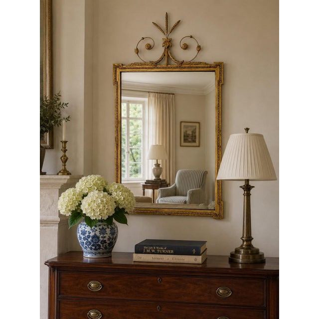 An elegant early-20th-century mirror in the Adam style, with a slender giltwood and composition frame crowned by an airy...